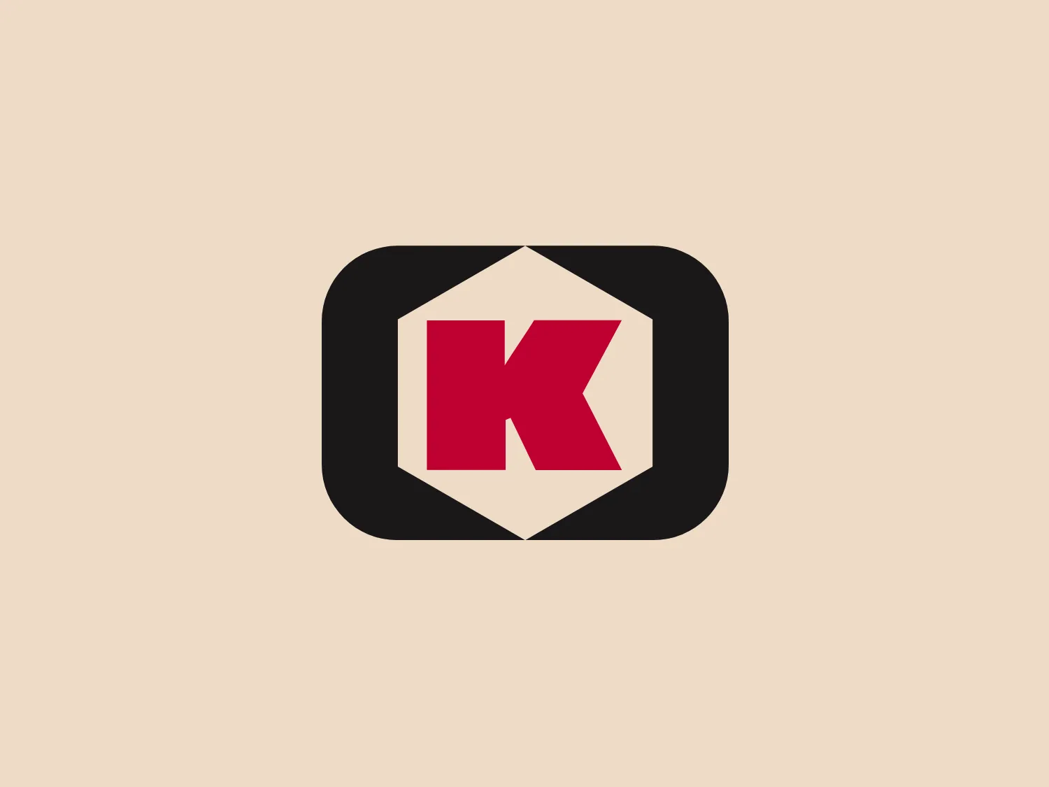 The Kongskilde logo features a bold, red "K" centered within a white hexagonal shape, which in turn is encapsulated by a rounded black rectangle. The "K" has a modern, blocky design with sharp angles, conveying a sense of solidity and strength. The stark contrast between the red and the black and white creates a striking visual impact. The rounded corners of the black background soften the overall design, making it contemporary and accessible.